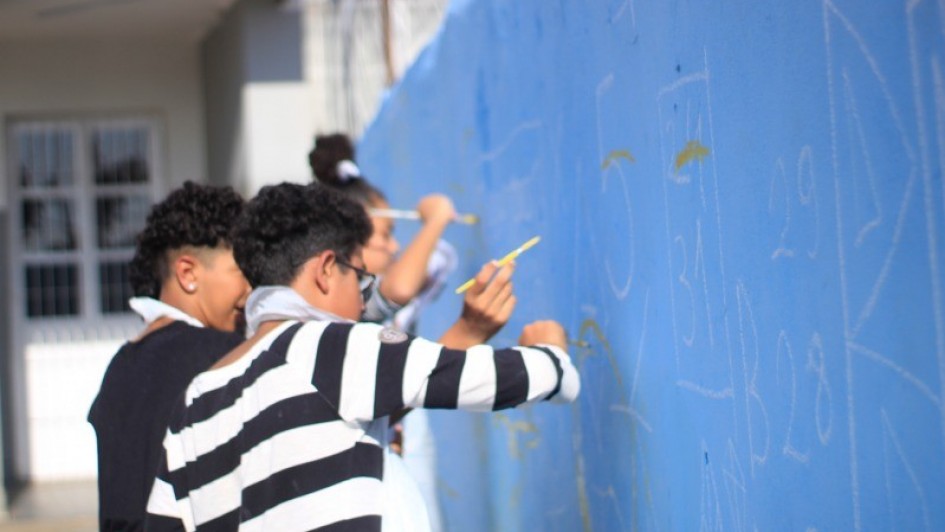 Dois adolescentes pintando numa parede azul 