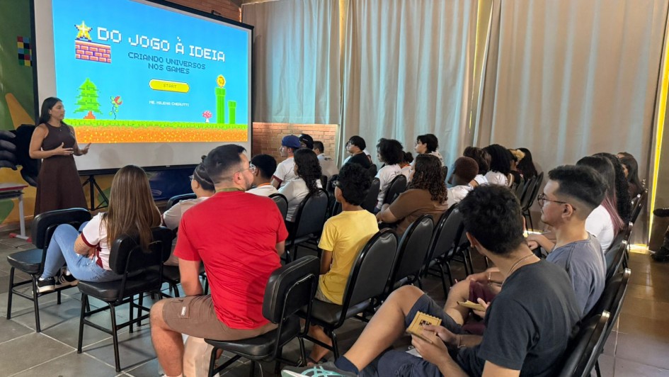 Fotos de uma sala de aula. No fundo tel&atilde;o com apresenta&ccedil;&atilde;o. A frente dele, a professora e na frente dela, em torno de 30 alunos sentados. 