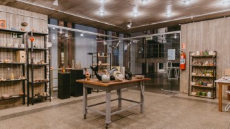 Imagem de sala com uma mesa no centro e estantes na volta, encostadas nas paredes. Na mesa e nas estantes, pe&ccedil;as de artesanato para venda.